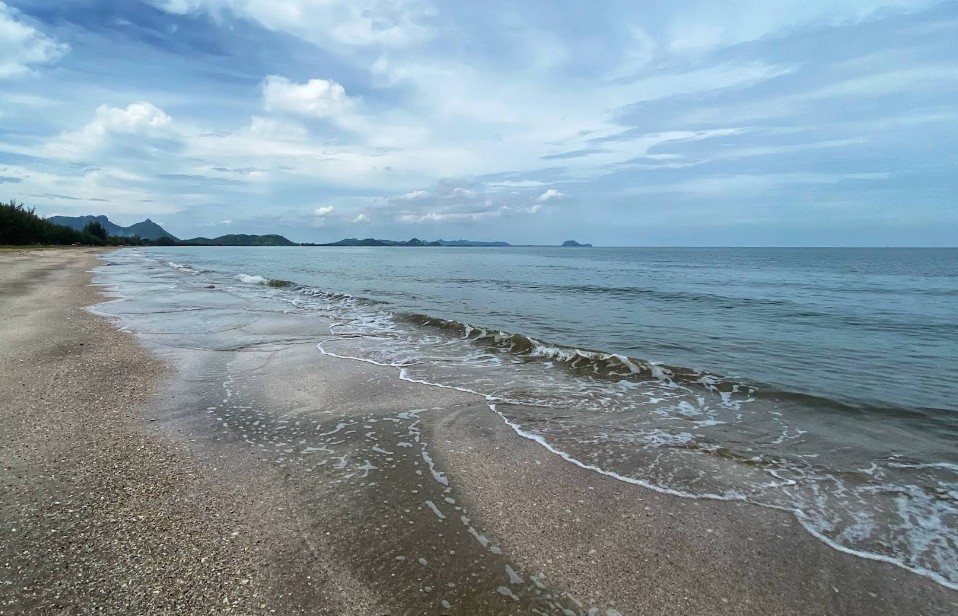 ป้ายหาดสามร้อยยอด อำเภอสามร้อยยอด สีดำตัวหนังสือสีทอง ตั้งอยู่บนชายหาดทรายขาว ขนาบข้างด้วยต้นมะพร้าว โดยมีวิวทะเลและภูเขาเป็นฉากหลัง