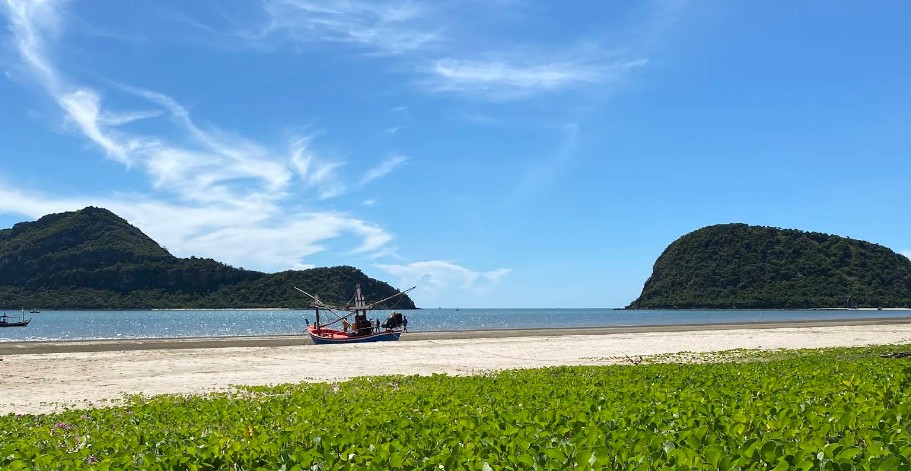 ป้ายหาดสามร้อยยอด อำเภอสามร้อยยอด สีดำตัวหนังสือสีทอง ตั้งอยู่บนชายหาดทรายขาว ขนาบข้างด้วยต้นมะพร้าว โดยมีวิวทะเลและภูเขาเป็นฉากหลัง