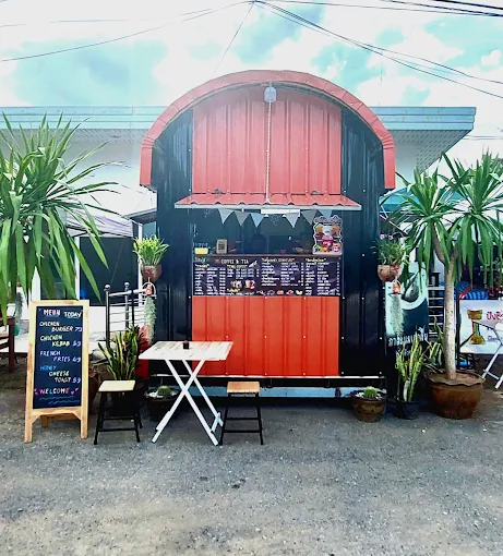 ซุ้มร้านกาแฟทรงโค้งสีส้มดำและที่นั่งเอาท์ดอร์หน้าร้าน Comfort Cafe ตกแต่งด้วยต้นจันทน์ผา