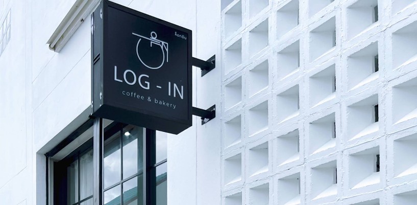 ป้ายหน้าร้านสีดำทรงสี่เหลี่ยม LOG-IN coffee & bakery ติดกับผนังบล็อกช่องลมสีขาวสไตล์มินิมอล