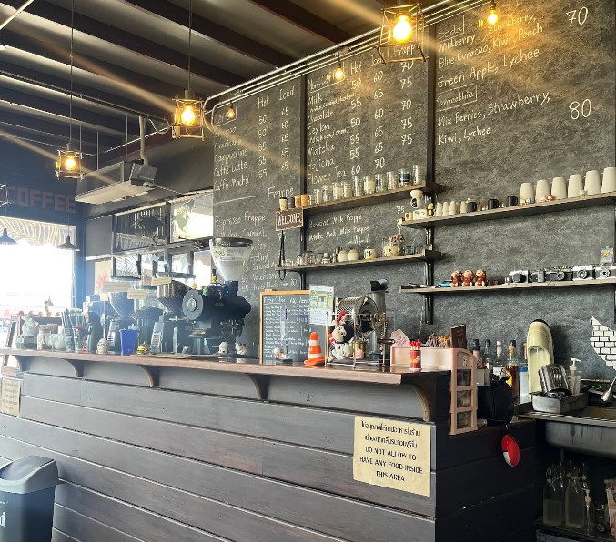 เคาน์เตอร์บาร์ไม้และผนังปูนเปลือยสไตล์ลอฟท์ที่ LoftFee Café ตกแต่งด้วยกระดานดำเมนูเครื่องดื่มและโคมไฟวินเทจ