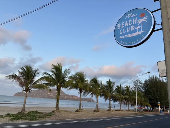 โซนที่นั่งริมทะเลพร้อมร่มชายหาดและบาร์เครื่องดื่มสีฟ้าของร้าน The Beach Club สามร้อยยอด