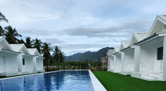 สระว่ายน้ำกลางแจ้งและบ้านพักวิลล่าสีขาวหลังเดี่ยวที่ The White เดอะไวท์ รีสอร์ท ด้านหลังเห็นวิวทิวเขาและต้นมะพร้าว