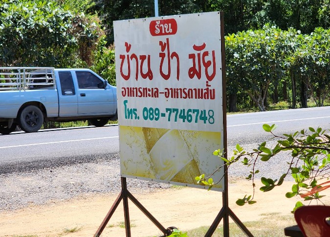 ป้ายทางเข้าร้านอาหารบ้านป้ามัย ตกแต่งด้วยหุ่นจำลองรูปปูและกุ้งริมถนนเลียบคลองธรรมชาติ